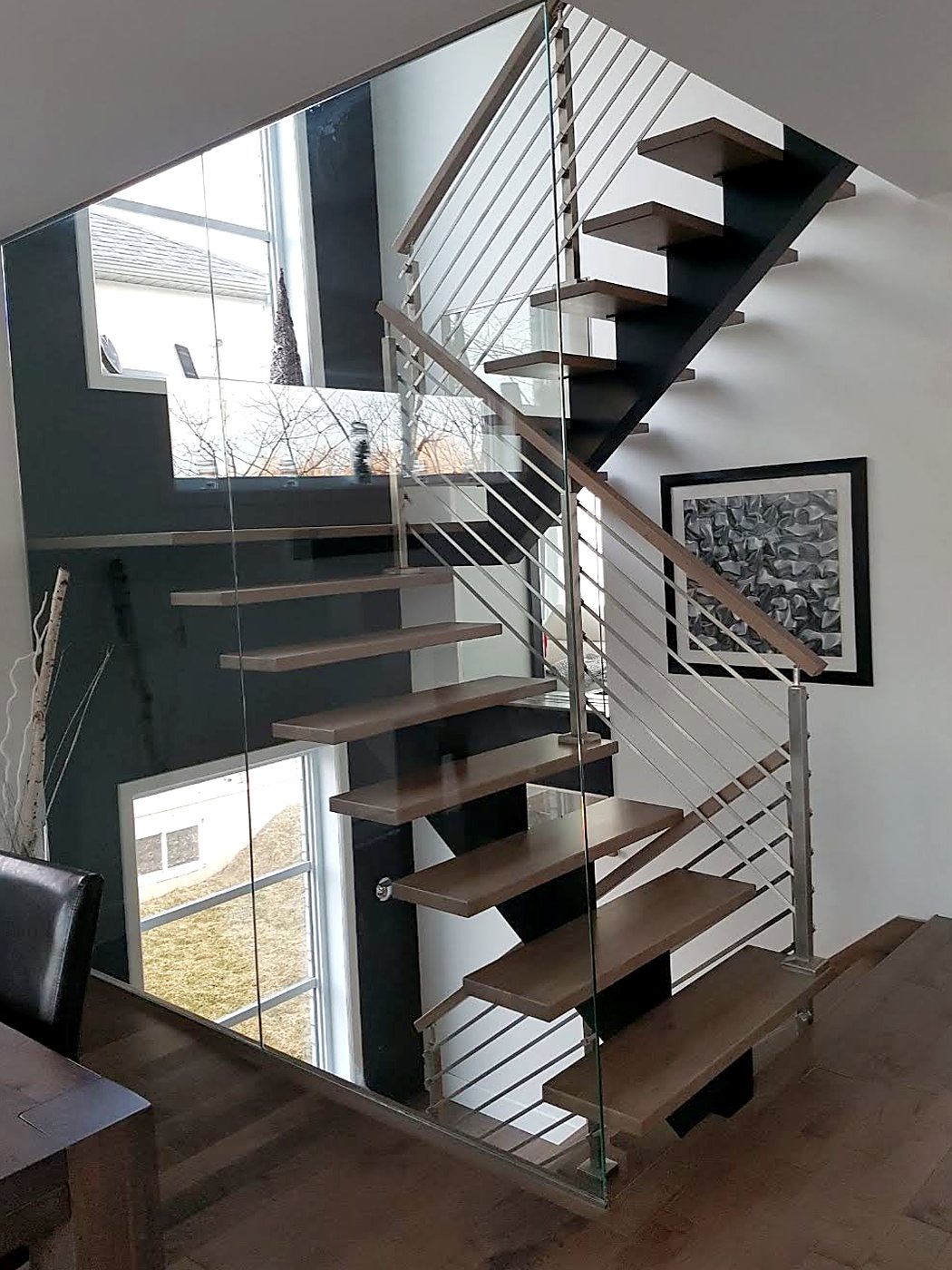 Escalier flottant en bois franc avec mur de verre et rampe en acier inoxydable
